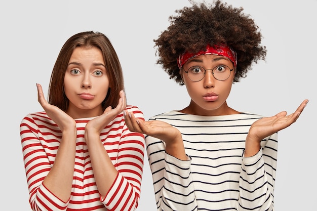 Free photo doubtful two young clueless girls spread palms, have uncertain facial expressions