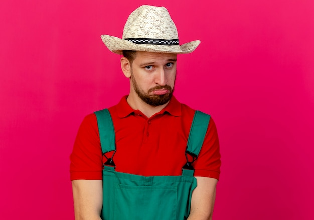 Free photo doubtful young handsome slavic gardener in uniform and hat looking