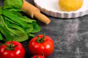 Free photo dough, greens and tomato on grey wooden table