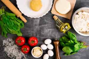 Free photo dough, oil, cheese, tomatoes, eggs, greens over grey wooden surface