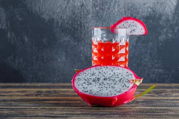 Dragon fruit with juice on wooden table and plaster wall, side view.