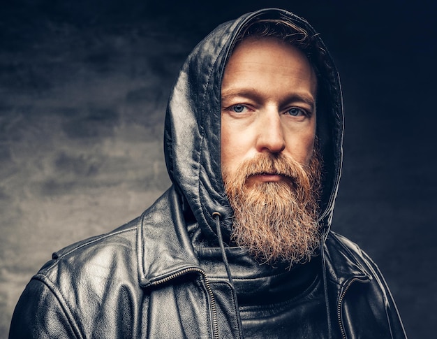 Free photo dramatic studio portrait of redhead bearded male dressed in a leather jacket over dark grey vignette background.