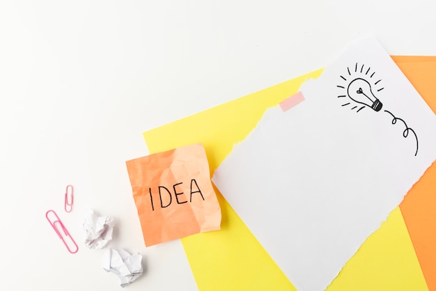 Free photo drawn light bulb and idea text written on sticky note with paperclip over white background