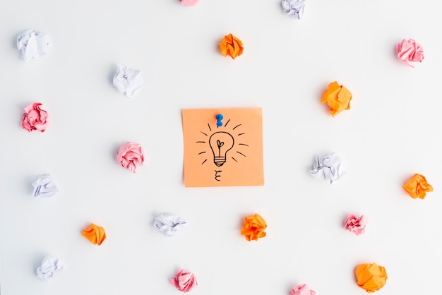 Drawn light bulb sticky note surrounded by crumpled paper over white surface