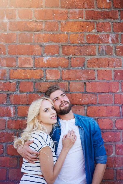 Dreaming couple standing next to brick wall