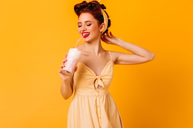 Dreamy attractive girl drinking milkshake. Romantic ginger woman enjoying beverage on yellow space.