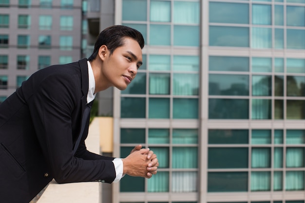 Free photo dreamy business man leaning on railing outdoors