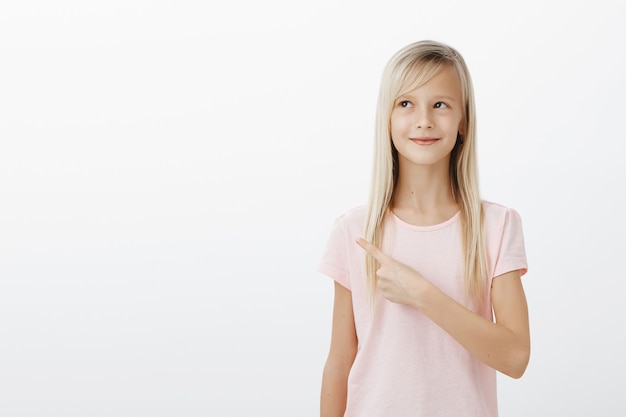 Dreamy cute blonde little girl pointing upper left corner pleased, imaging or thinking