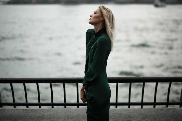 Free photo dreamy girl in green dress stands on the embankment