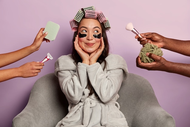 Free photo dreamy happy woman poses with eyes patches and curlers