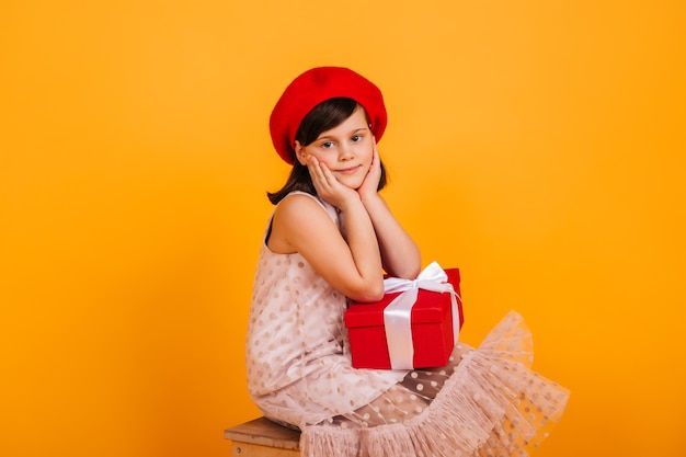 Dreamy kid posing with birthday present. Preteen girl in red beret holding new year gift.