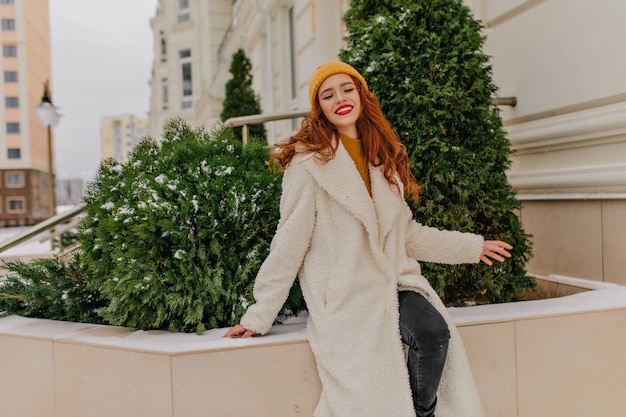 Free photo dreamy red-haired woman posing on the street in winter day. outdoor photo of merry caucasian girl expressing positive emotions.