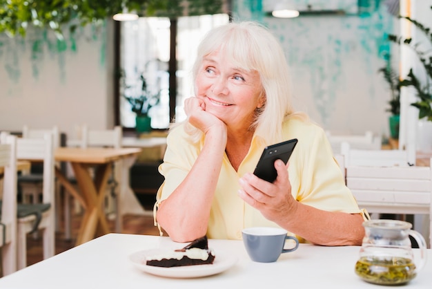 Dreamy smiling elderly woman with smartphone