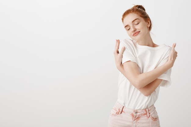 Dreamy tender redhead woman embracing own body, daydreaming