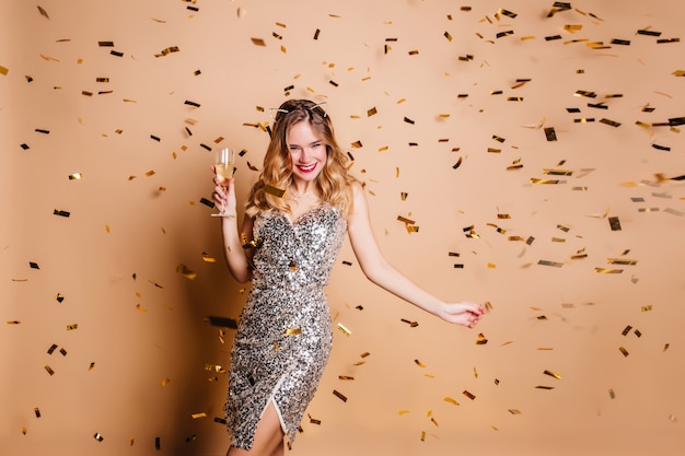 Free photo dreamy woman in elegant sparkle dress dancing with wineglass and smiling