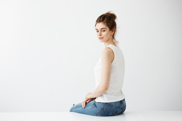 Free photo dreamy young beautiful brunette woman with bun smiling thinking sitting over white background.