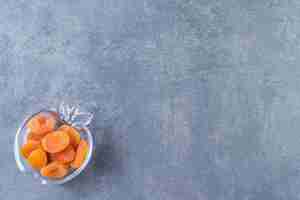 Free photo dried apricot in a glass bowl , on the marble background.