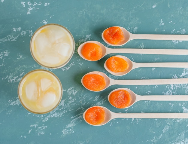 Free photo dried apricots in a wooden spoons with juice top view on a plaster wall