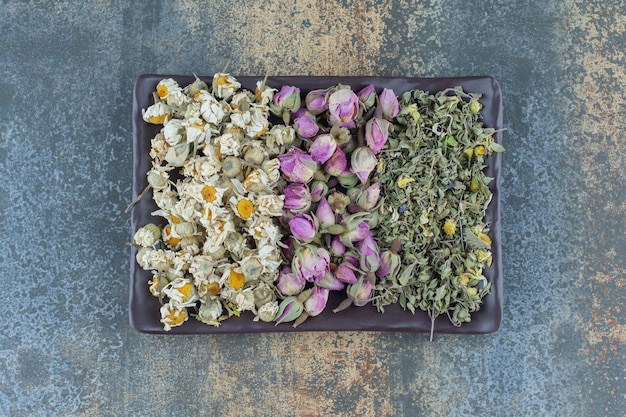 Dried chamomile, rose and leaves on dark plate.