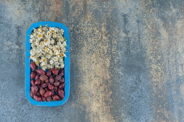 Dried chamomile and rosehips on blue plate.