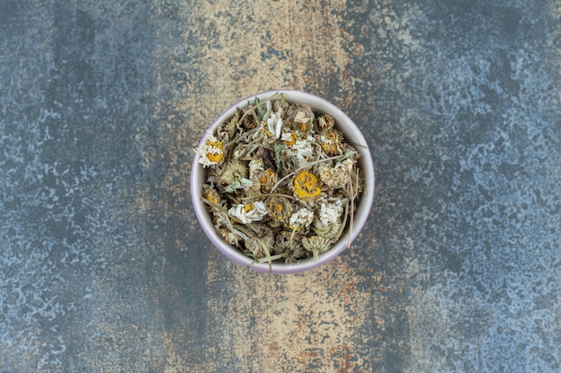 Dried chamomile tea in purple bowl.