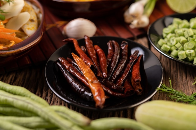 Dried chilies fried in a black plate with lentils Cucumbers and garlic are placed on the wooden table.