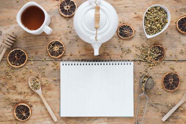 Dried chinese chrysanthemum flowers; teapot; dried orange; tea strainer; honey dipper; bowl and fresh lemon tea with blank spiral book