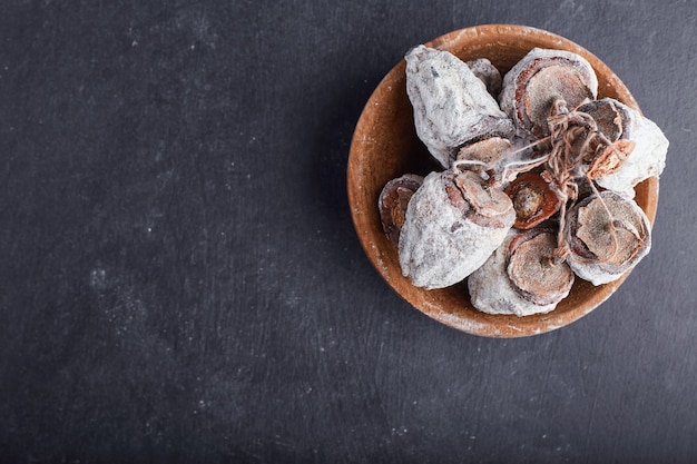 Dried date plums in a wooden cup on grey surface, top view. 