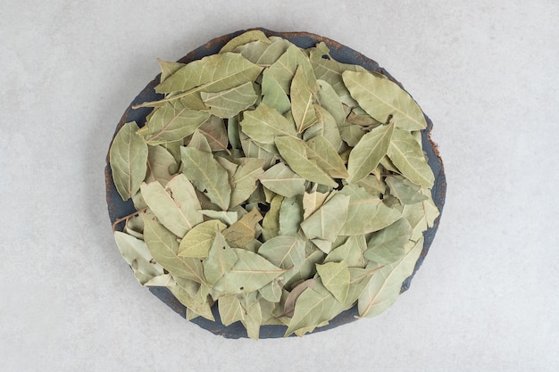 Dried green bay leaves on a wooden plate.