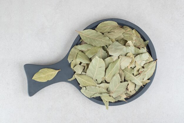 Dried green bay leaves on a wooden plate.