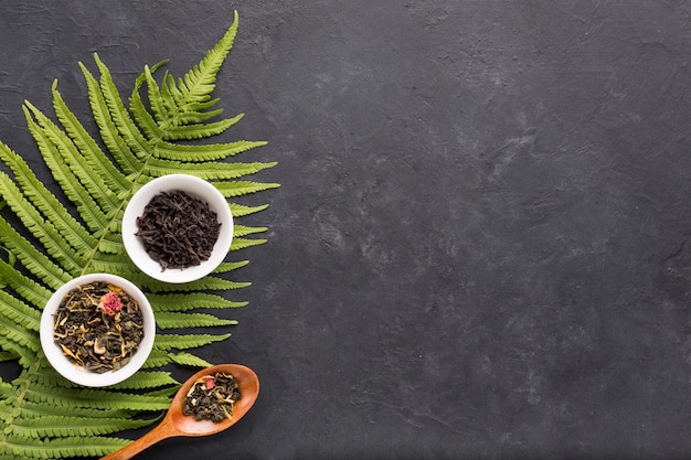 Free photo dried herb tea in white ceramic bowl with fern leaves on black background