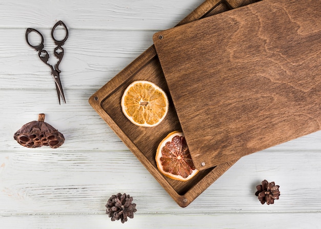 Free Photo dried orange; grapefruit slice; lotus pod; pinecone with scissor on white wooden table