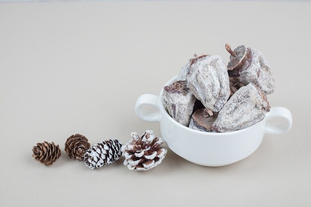 Free photo dried persimmon bowl and pinecone on beige surface