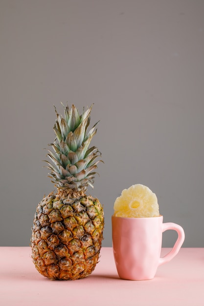 Free Photo dried pineapple in a cup with fresh pineapple on pink and grey surface