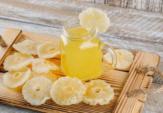 Dried pineapples with juice in a tray on wooden surface