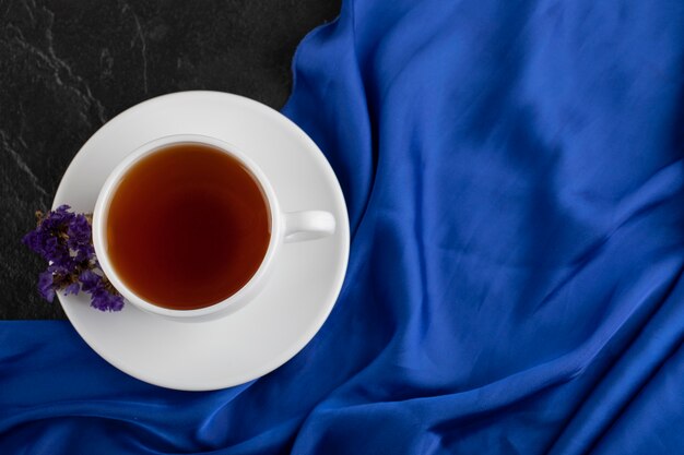 Dried purple flowers with a cup of hot tea on a black table . 