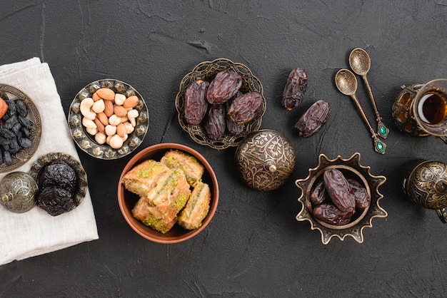 Free photo dried raw organic dates; nuts and baklava on metallic iron plate over the black backdrop