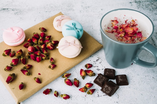 Free photo dried rose buds; macaroons and chocolate pieces on board with cup