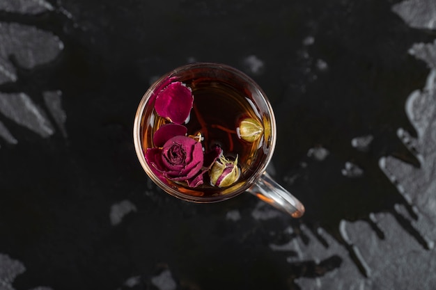 Free photo dried rose in a cup of hot tea on a black table .