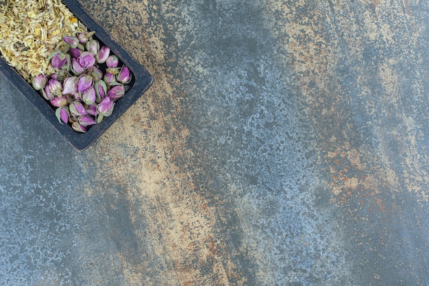 Dried roses and daisies on black plate.