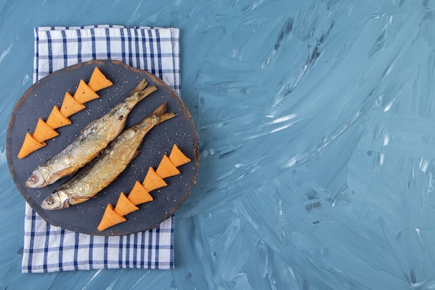 Free photo dried salted sprat and cone chips on a board on a towel, on the marble background.