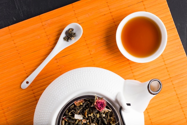 Dried tea herb and tea on place mat with ceramic teapot