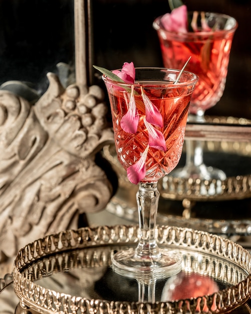 A drink in a glass with rose petals on a tray