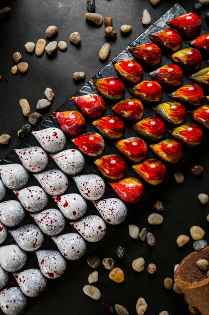 Drop form chocolates on the black board red yellow white seastones top view