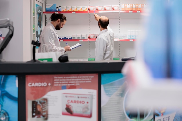 Free photo drugstore employee looking at drugs packages while working at pills inventory in pharmacy. pharmacists is trained in pharmacology and is able to fill and dispense prescription medication accurately.