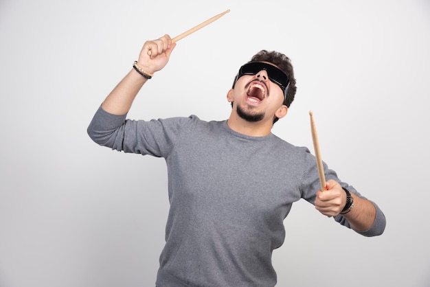 A drummer in black sunglasses holding drum sticks and looks very energic.