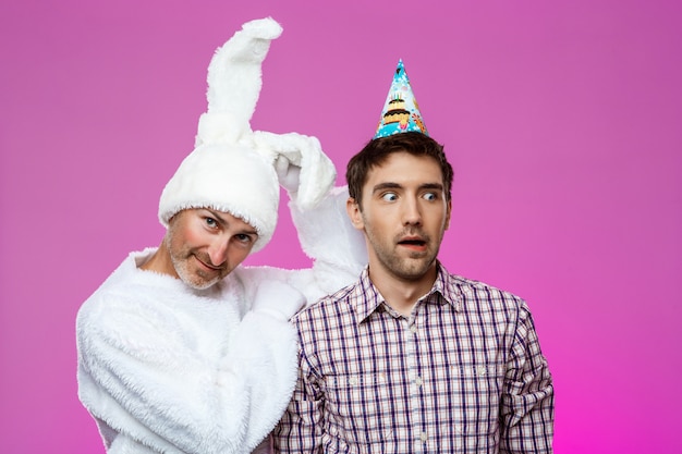 Drunk man and rabbit at birthday party over purple wall.