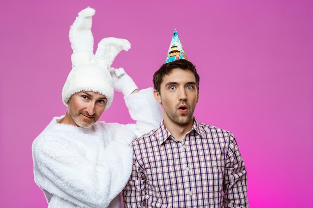 Drunk man and rabbit at birthday party over purple wall.