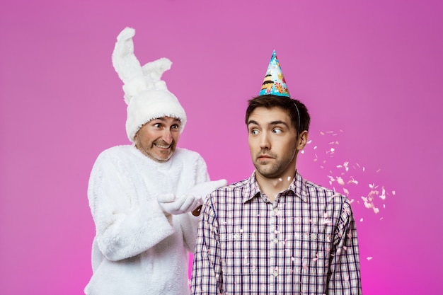 Drunk man and rabbit at birthday party over purple wall.