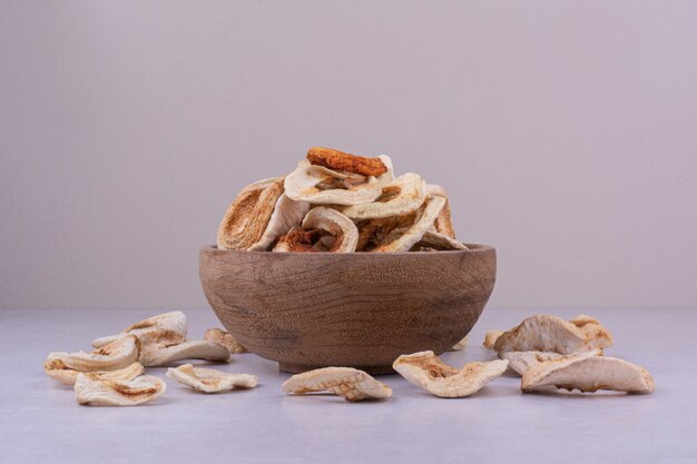 Dry apple slices in a wooden cup on grey surface